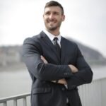 Smiling businessman in a suit standing confidently outdoors by the river.
